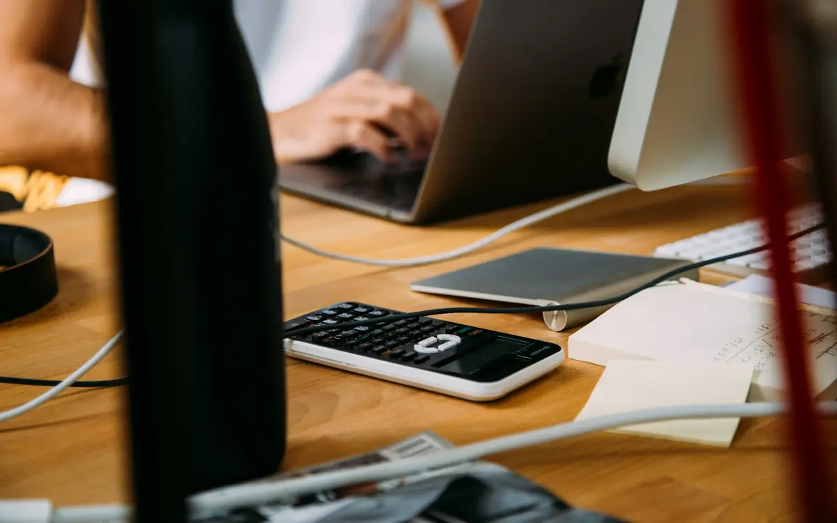Calculator, laptop and paperwork on an office desk, representing payroll and software cost calculations
