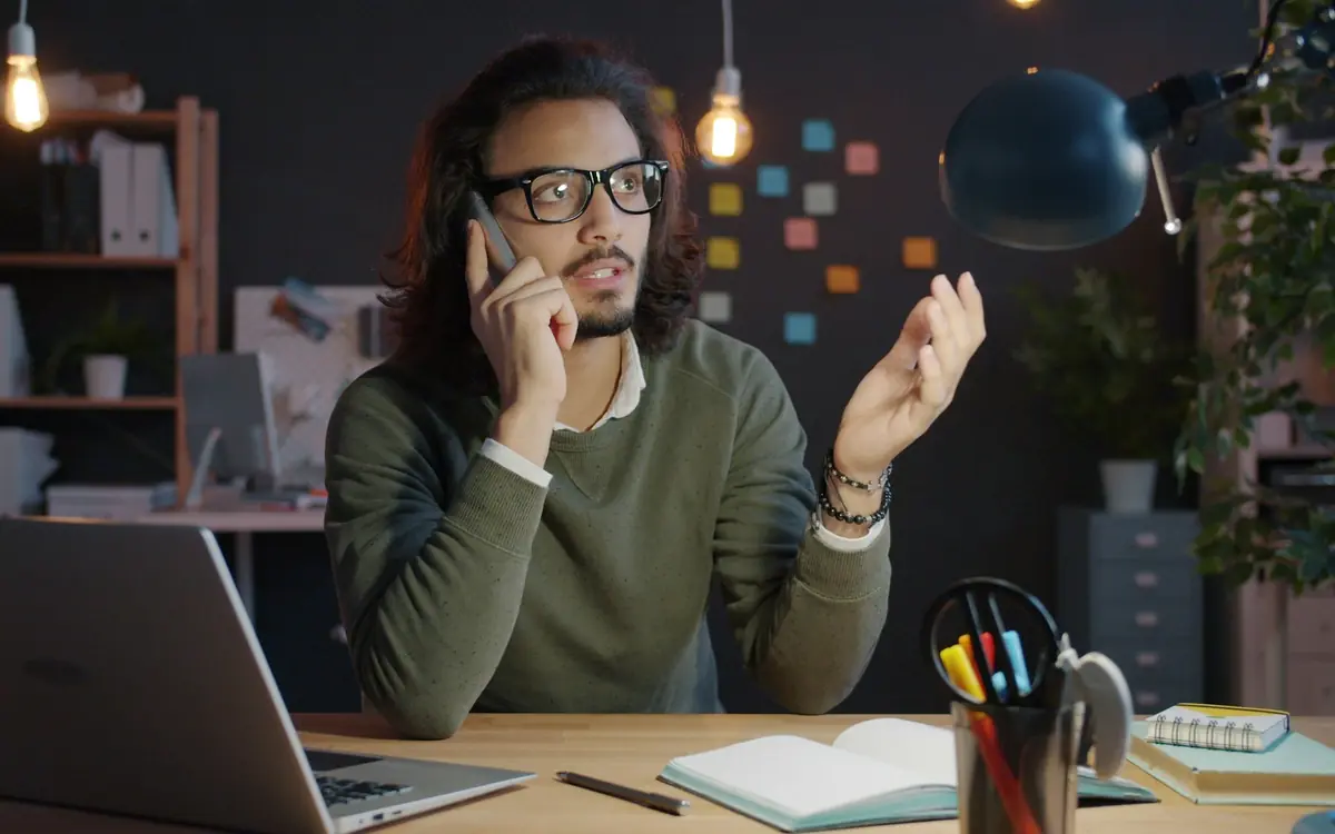 Sales manager talking on his phone at a desk with a laptop and notebook while following up a customer lead
