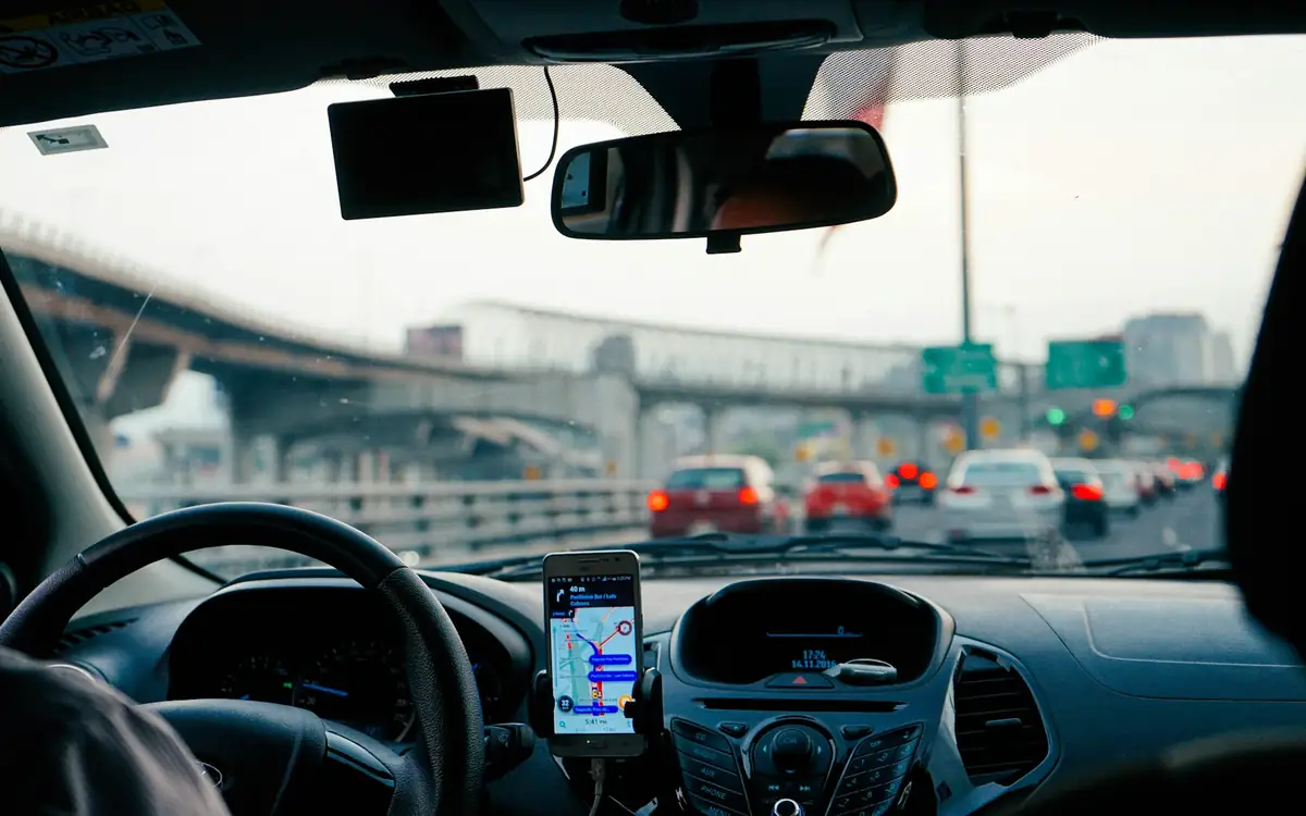 Car dashboard with a phone mounted showing a live GPS navigation map while driving through city traffic