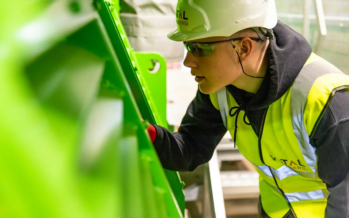 Worker in a white hard hat, safety glasses and high-visibility vest inspecting equipment on site